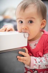 Portrait of cute baby girl biting table while sitting at home