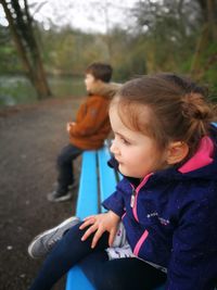 Siblings sitting on bench in forest