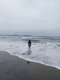 Rear view of teenage girl standing on shore at beach against sky