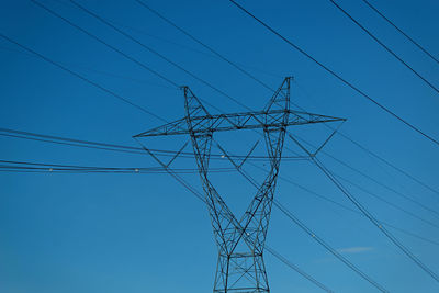 Low angle view of electricity pylon against clear blue sky