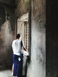 Rear view of woman standing by window in abandoned building