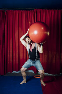 Male circus acrobat carrying red ball while performing on stage