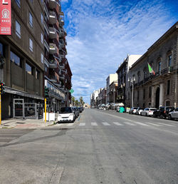 Cars on road by buildings in city against sky