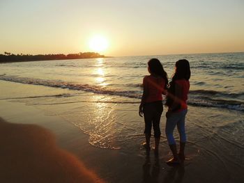 Rear view of friends standing on beach during sunset