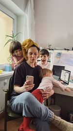 Woman wearing a yellow towel working  with a laptop and a smartphone surrounded with three children