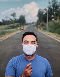 Portrait of man holding flower and wearing mask on road