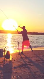 Rear view of silhouette man standing at beach during sunset