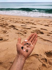 Cropped image of hand on sand at beach against sky