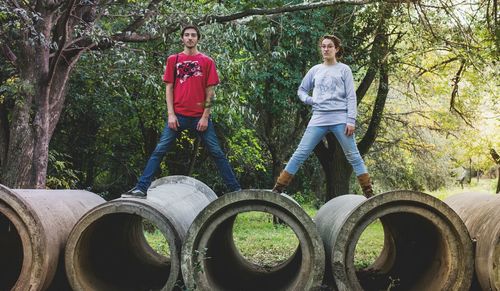 Full length portrait of friends standing on abandoned pipes in forest