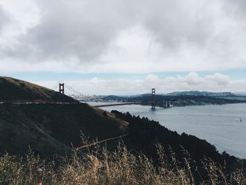View of suspension bridge over sea against cloudy sky