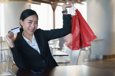 Portrait of smiling young woman holding credit card and shopping bags
