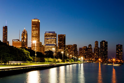 Illuminated buildings by river against sky in city