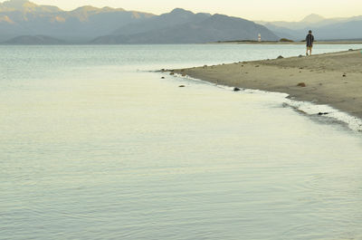 Kids walk along beach to distant lighthouse at dusk