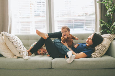 Happy mother playing with children on sofa at home