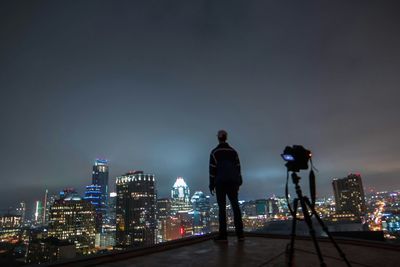 Rear view of a man overlooking illuminated cityscape