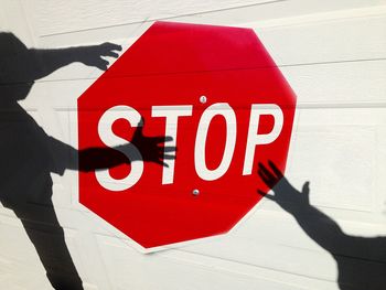 Optical illusion of shadows holding stop sign painted on white wall