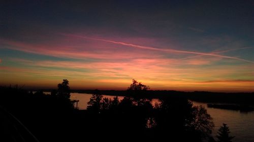 Silhouette trees by lake against sky during sunset
