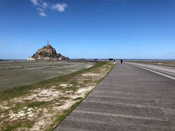 View of footpath leading towards building against clear blue sky