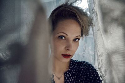 Close-up portrait of young woman against curtain at home