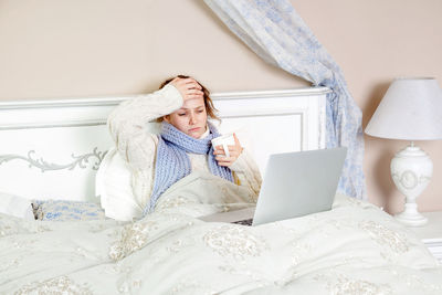 Young woman using mobile phone while sitting on bed