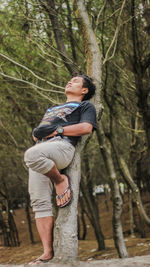 Low angle view of man leaning against tree trunk