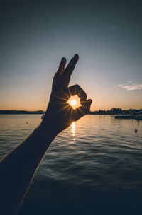 Person hand holding sea against sky during sunset