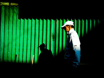 Side view of man standing against wall at night