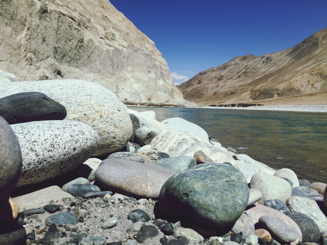 rock - object, stone - object, mountain, blue, sky, water, nature, tranquility, pebble, sunlight, scenics, stone, beauty in nature, rock, day, tranquil scene, clear sky, outdoors