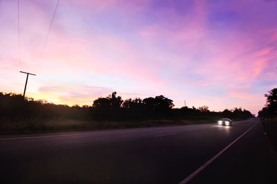 Silhouette trees by road against sky during sunset