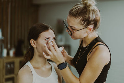 A young makeup artist applies a medicinal liquid under a girl s eyes.