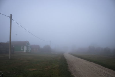 Road amidst field against sky during foggy weather