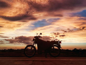Bicycle on road against dramatic sky during sunset