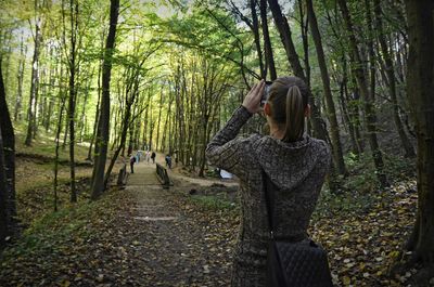 Rear view of woman photographing while standing in forest