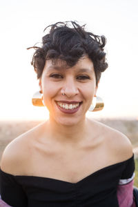 Black short haired female teenager with earrings and piercing laughing and looking at camera on blurred background of nature