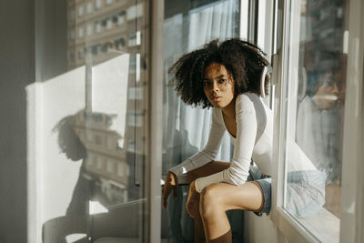 Confident woman with curly hair sitting on window sill at home