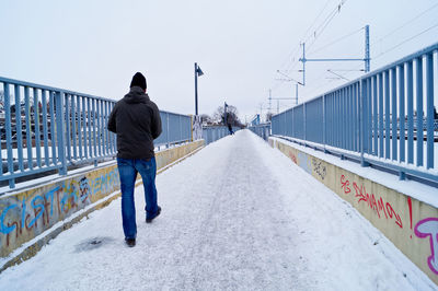 Rear view of woman walking on snow covered footbridge against sky