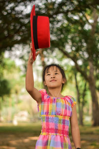 Cute little girl throwing a red hat in a summer green park.