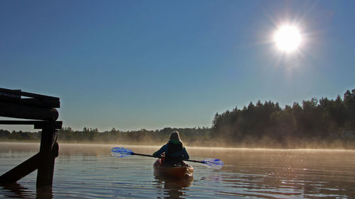 Rear view of people rowing boat in lake against sky