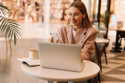 A business woman with glasses works and studies online using a mobile phone and technology in a cafe