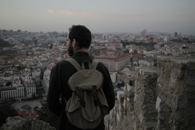 Rear view of man with backpack looking at cityscape during sunset