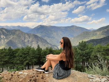 Side view of young woman sitting on mountain against sky