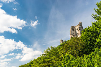 The ruins of a historical tower on a hill covered with trees in the background of blue sky