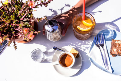 Cropped image of woman holding container by drink and vase at table