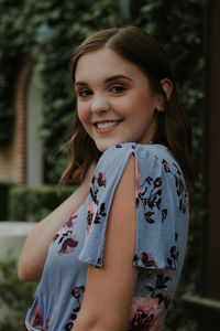 Portrait of smiling young woman standing against plants in park