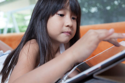 Close-up of girl using digital tablet while lying down on sofa at home