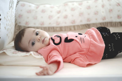 Portrait of cute baby girl lying on bed at home