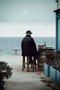 Rear view of man sitting on chair at beach