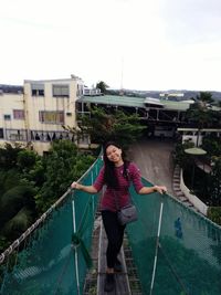 Portrait of smiling woman standing on footbridge against sky