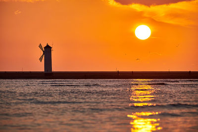 Silhouette man standing on sea against sky during sunset