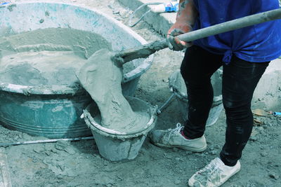 Low section of woman pouring concrete in bucket at construction site